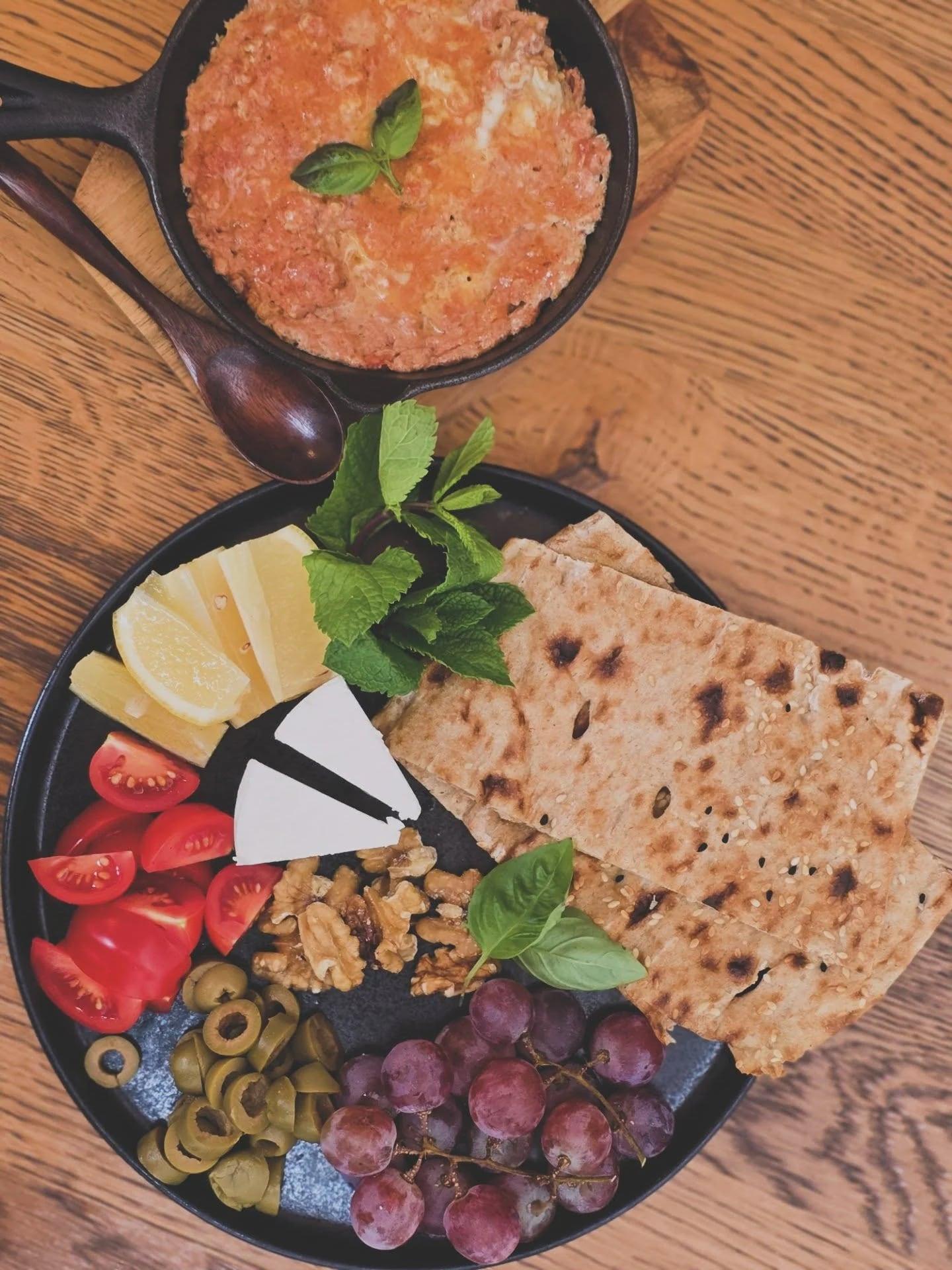 Omelette persane dans une poêle en fonte avec pain plat, fromage blanc, noix, raisins et menthe